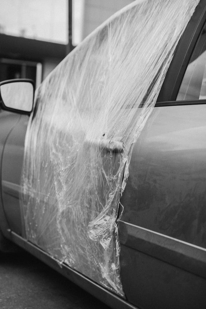 A grayscale image of a car door repaired with plastic wrap, showcasing temporary solutions.